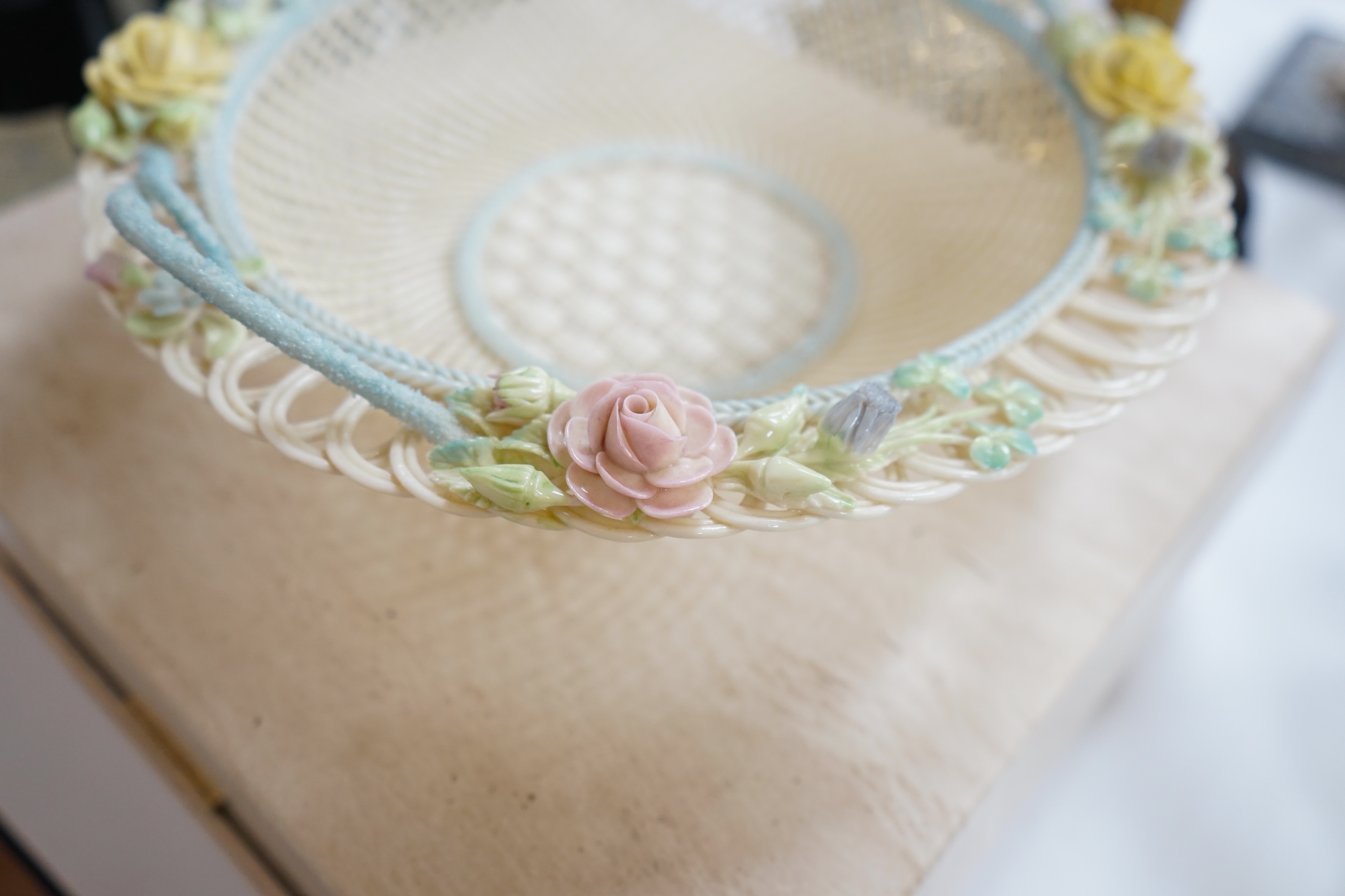 A boxed Belleek coloured basket, 28cm diameter. Condition - fair to good, some damage and wear to the box.